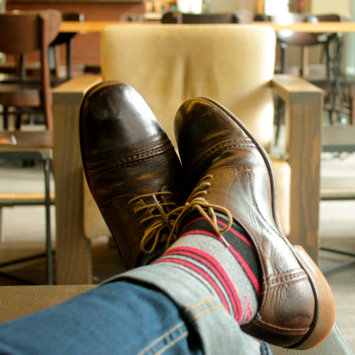Grey, black, and red stiped socks with brown shoes and jeans