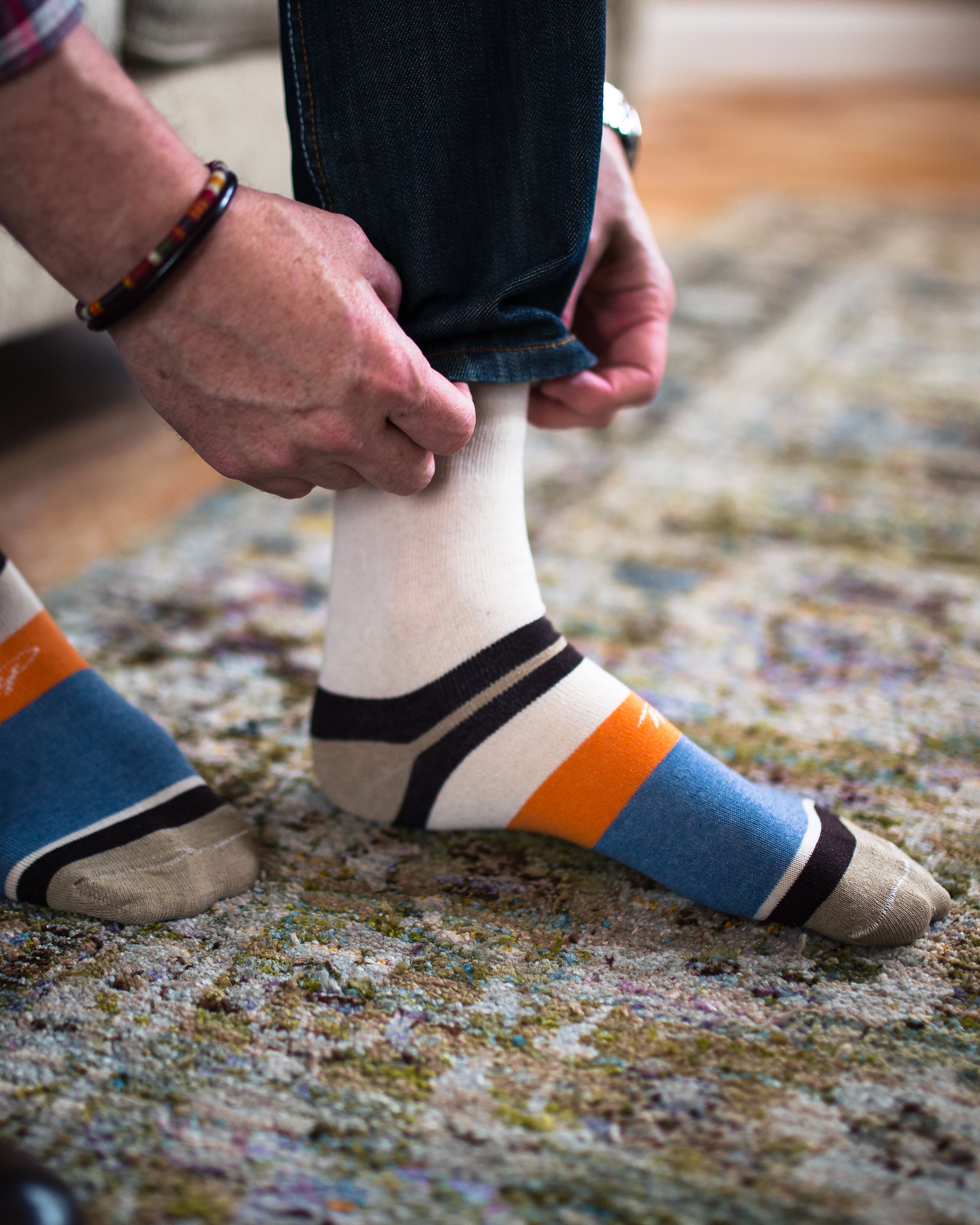 beige over the calf dress socks with orange and light blue stripes on foot and light brown toe and heel, dark blue jeans
