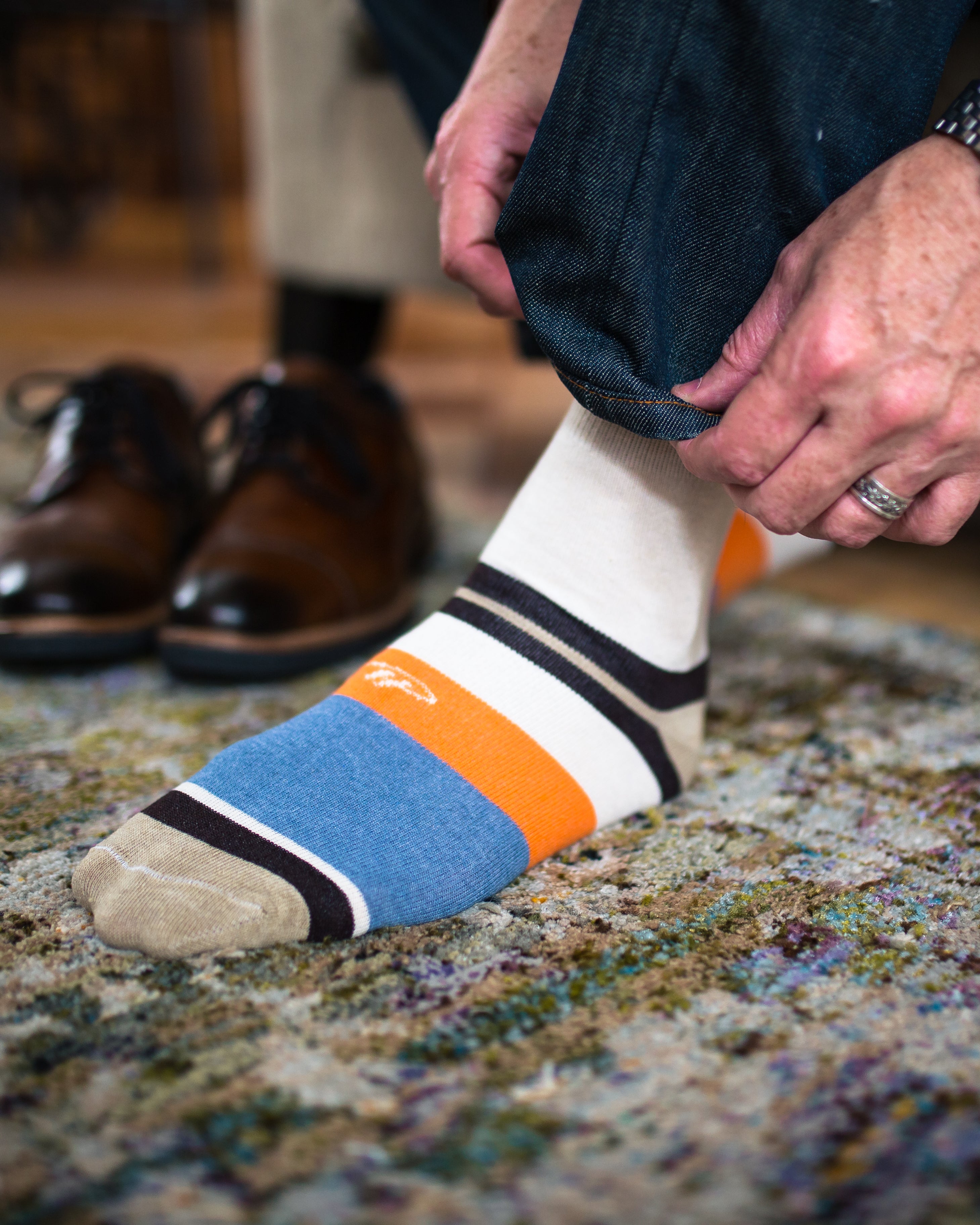 beige over the calf dress socks with orange and light blue stripes on foot and light brown toe and heel, dark blue jeans