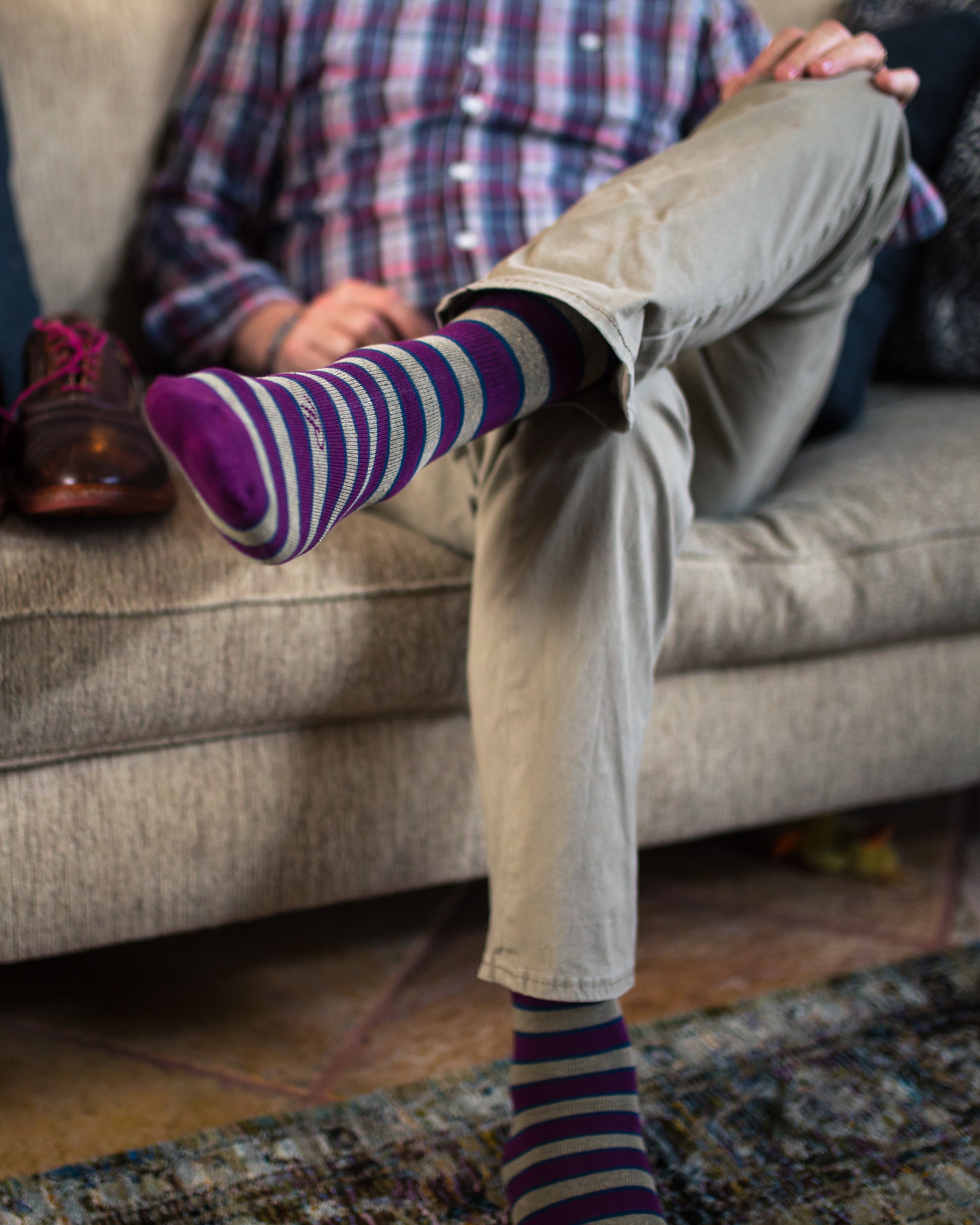 brown and burgundy striped over the calf dress socks, khaki pants, crossed leg, brown dress shoes with pink laces on couch