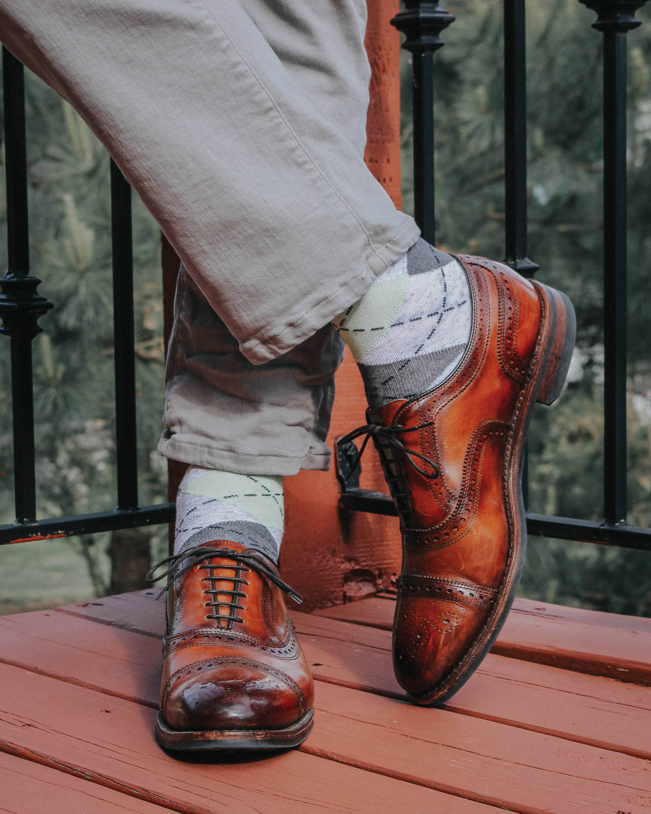 grey argyle over the calf dress socks, with brown dress shoes, grey pants, on a wooden floor