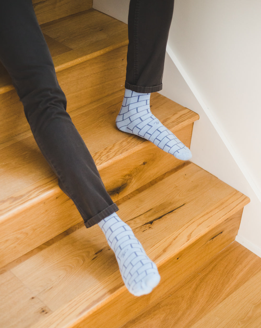 light grey over the calf dress socks with blue brick patterned lines, black pants, on wooden staircase