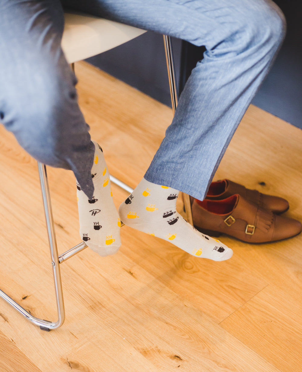 light grey over the calf dress socks with yellow and black hot coffee mug prints, grey dress pants, brown dress shoes on floor, chair