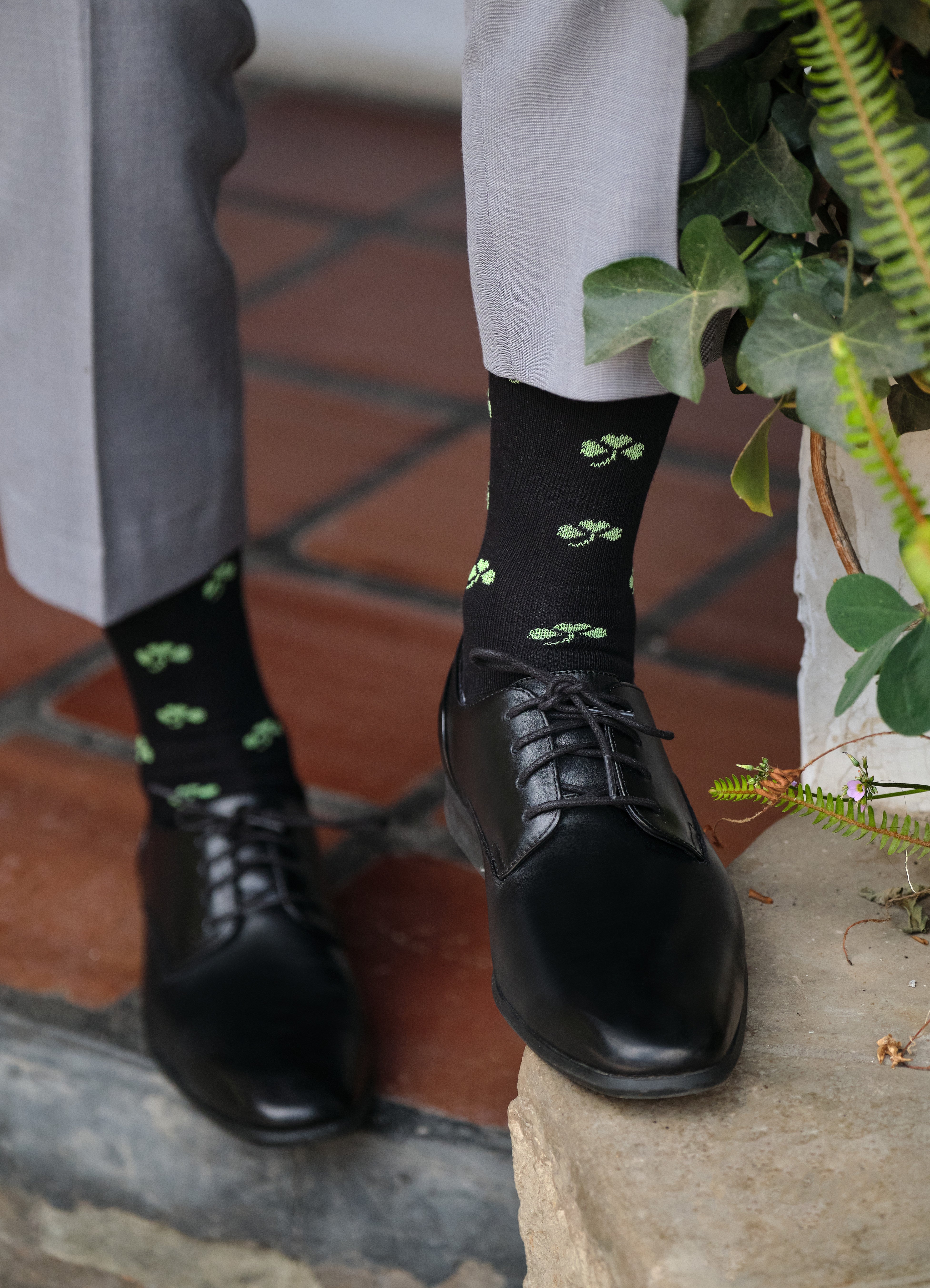 black mid calf dress socks with green clover prints, black dress shoes, light grey dress pants
