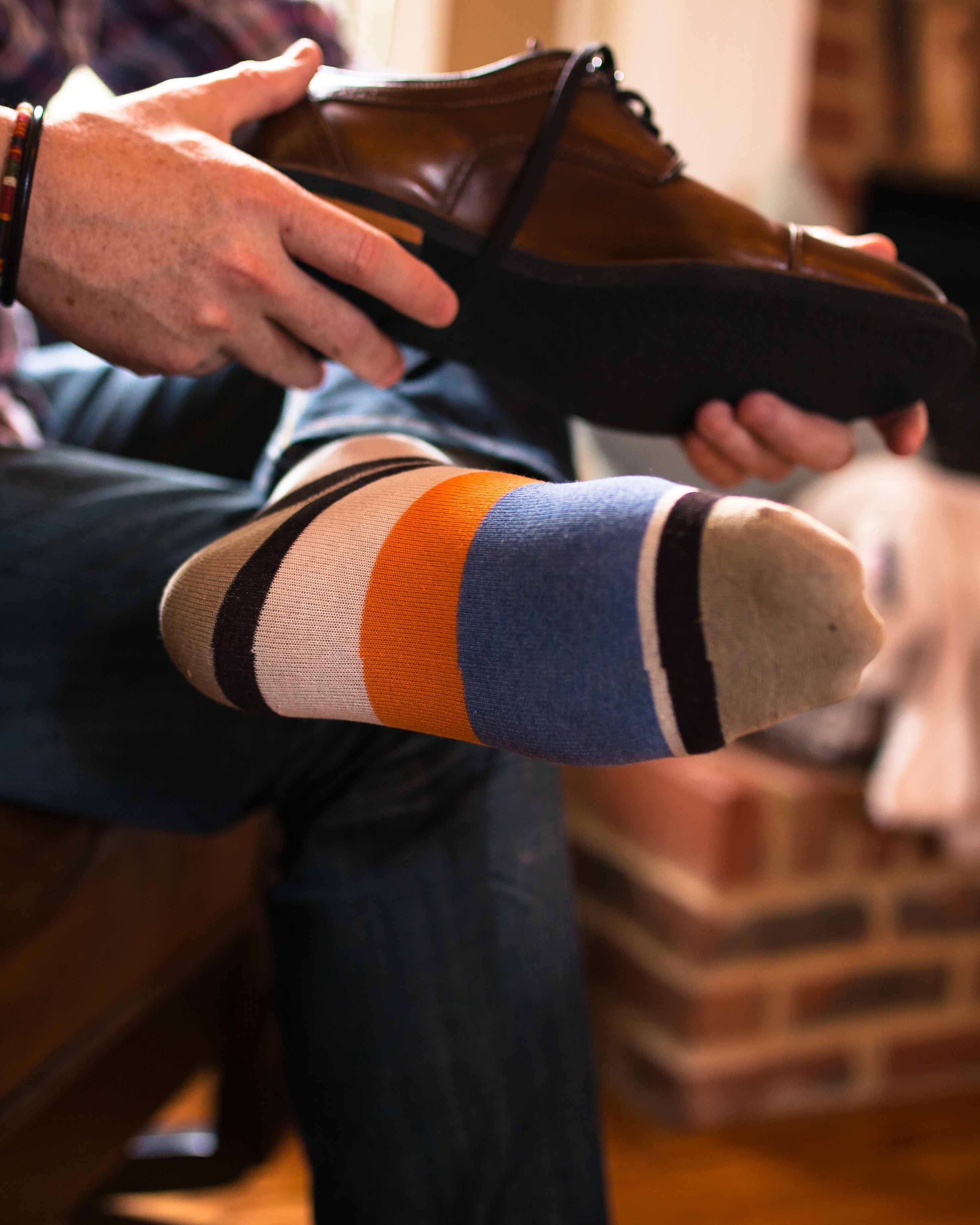 beige over the calf dress socks with orange and light blue stripes, holding brown dress shoes