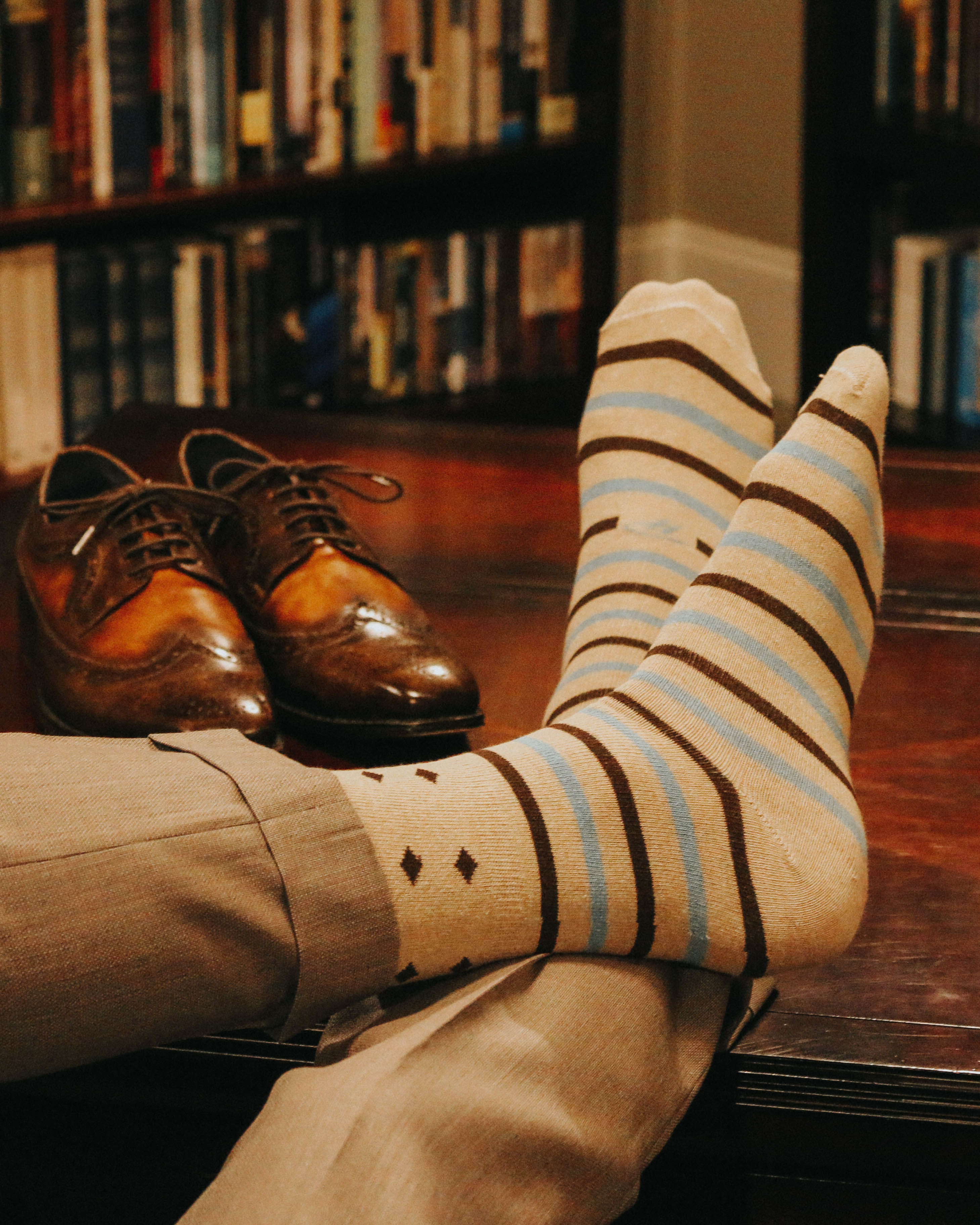 beige over the calf dress socks with light blue and brown stripes, brown dress shoes, light brown dress pants, on a wood table