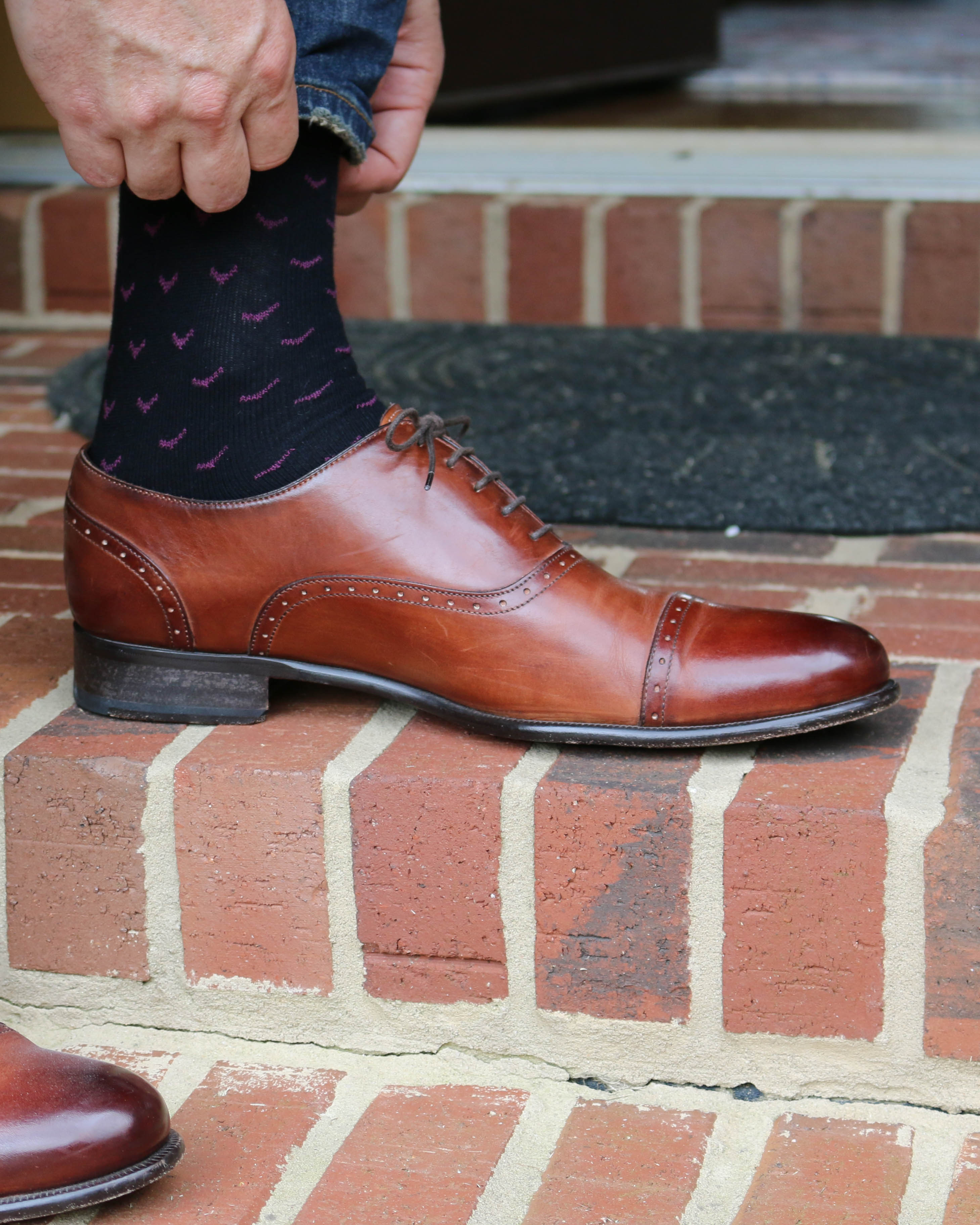 black over the calf dress socks with pink print, blue jeans, a brown dress shoe