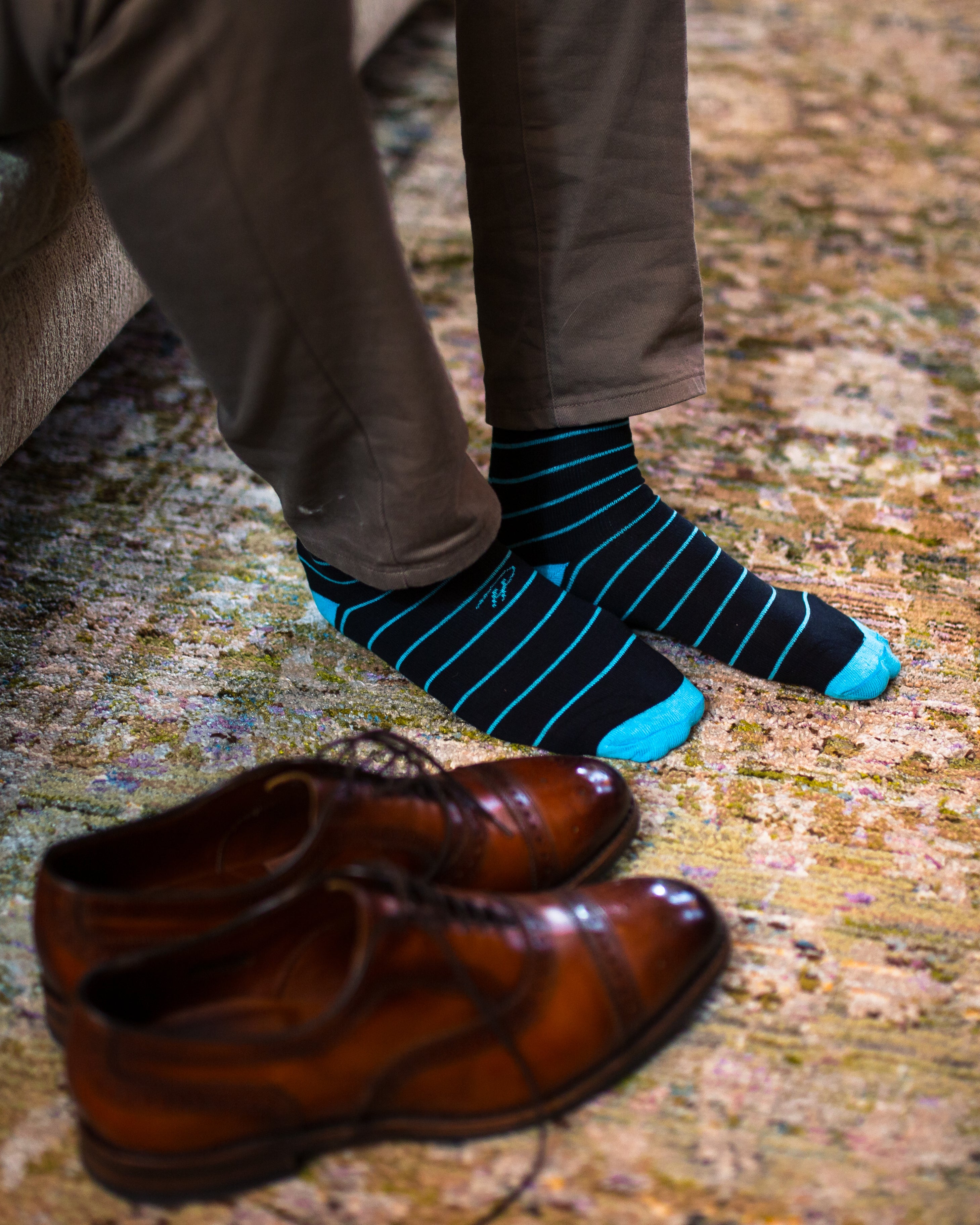 black over the calf dress socks with light blue stripes, brown dress shoes on the floor, grey pants