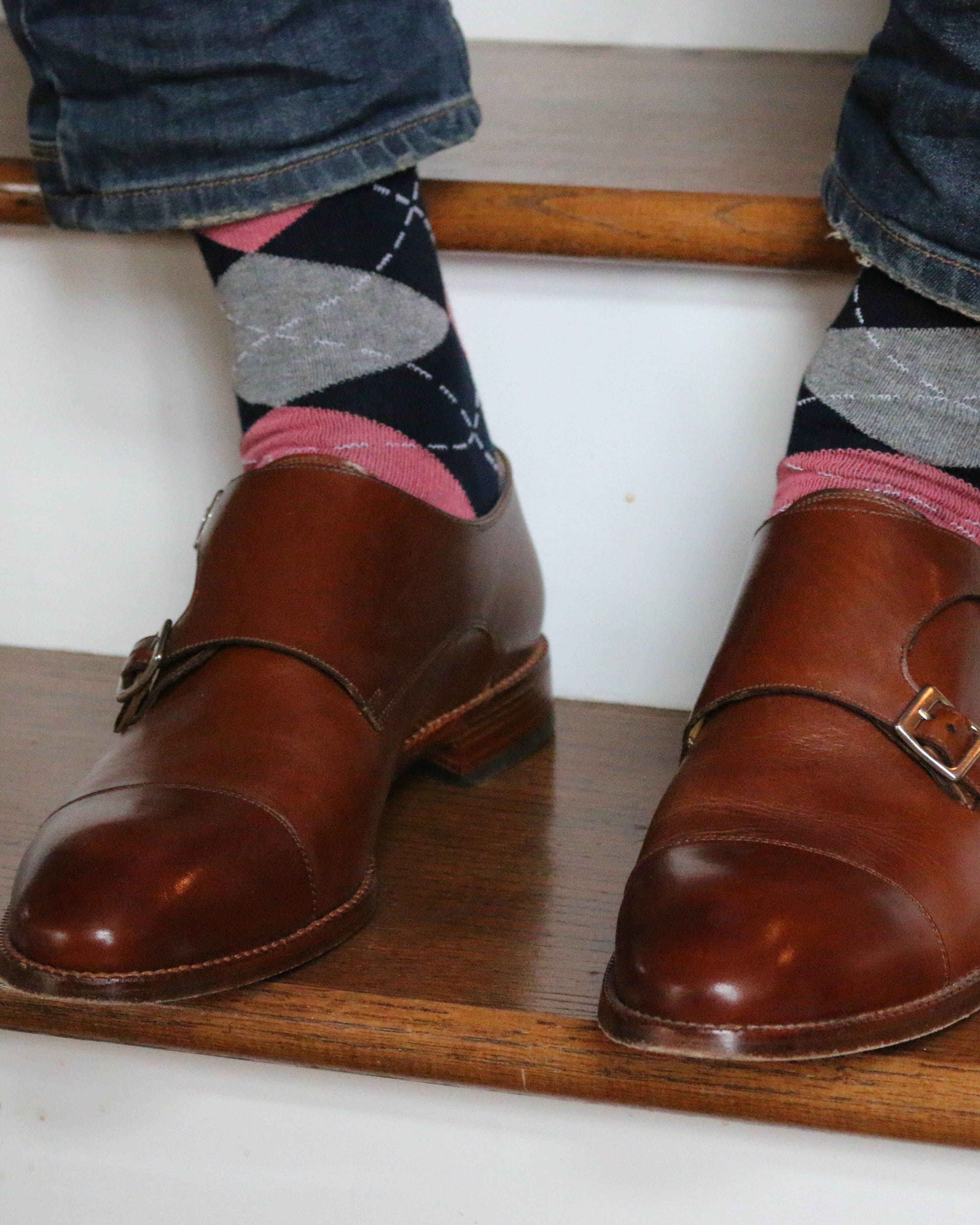 blue pink and grey argyle print over the calf dress socks, brown dress shoes, blue jeans, on stairs