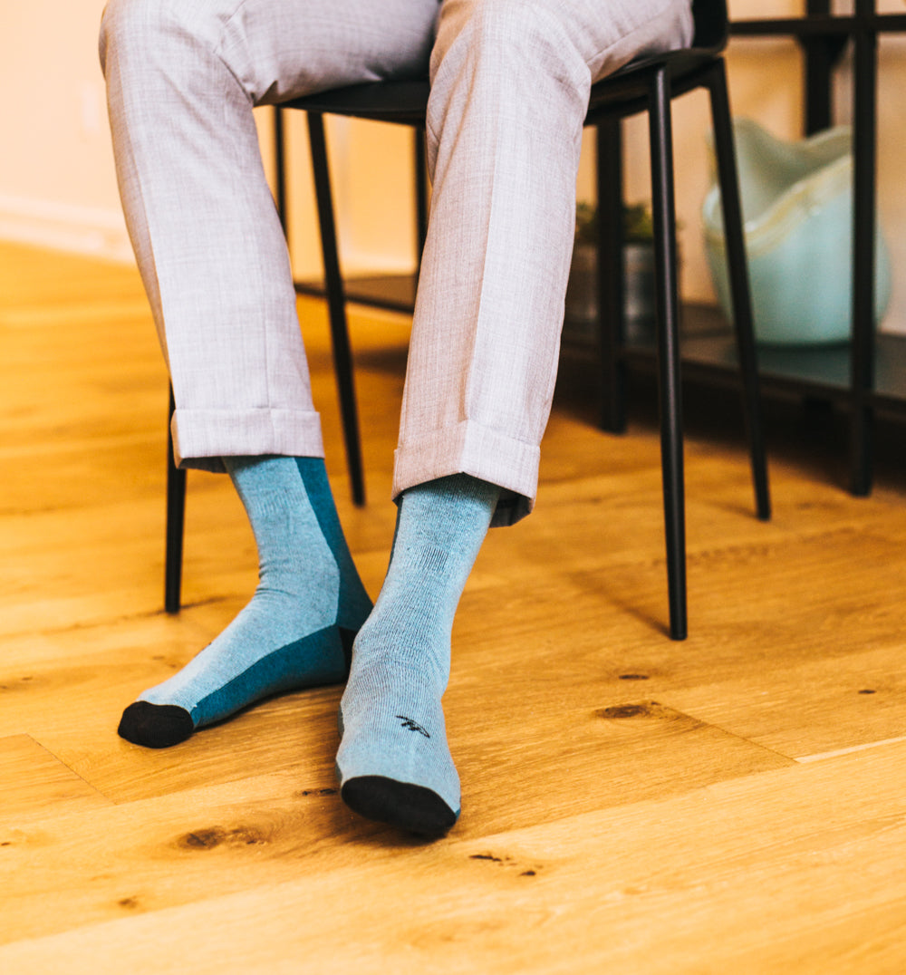 light blue over the calf dress socks with blue stripe and black toe and heel, grey dress pants, a black chair