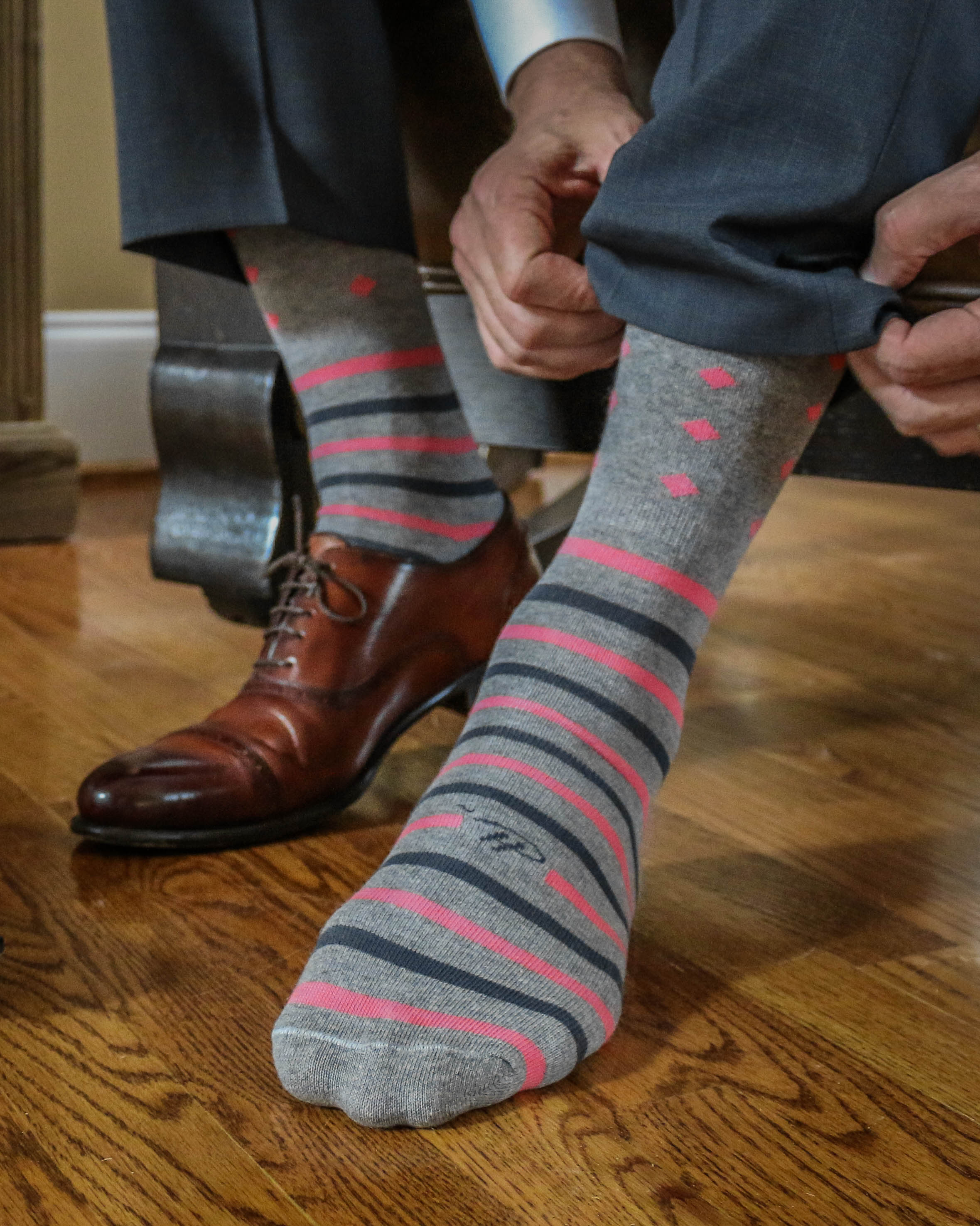 light grey over the calf dress socks with pink and grey stripes and pink diamonds, brown dress shoe, grey dress pants, a wooden floor