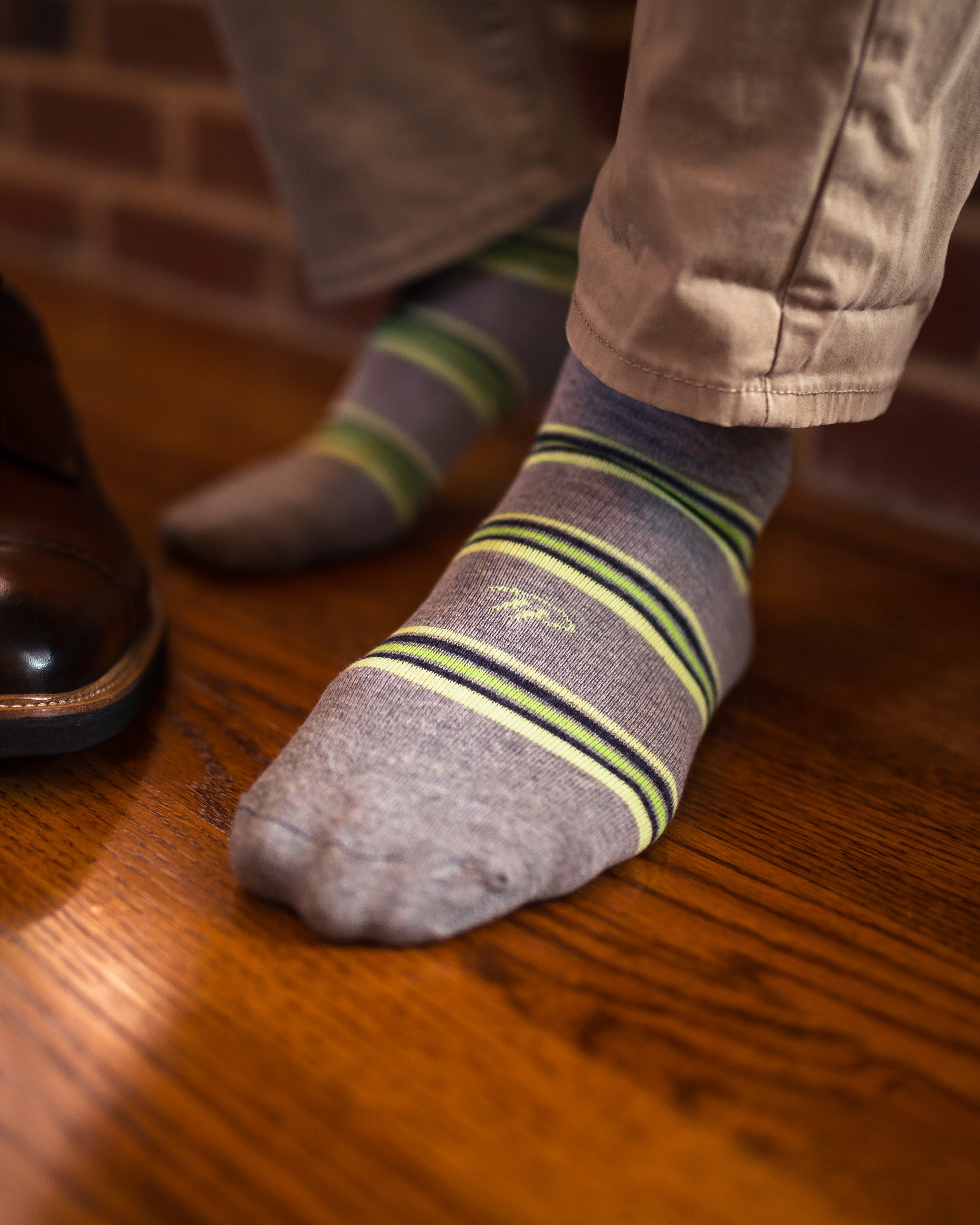 light grey over the calf dress socks with green stripes, brown dress shoe on floor, khaki pants