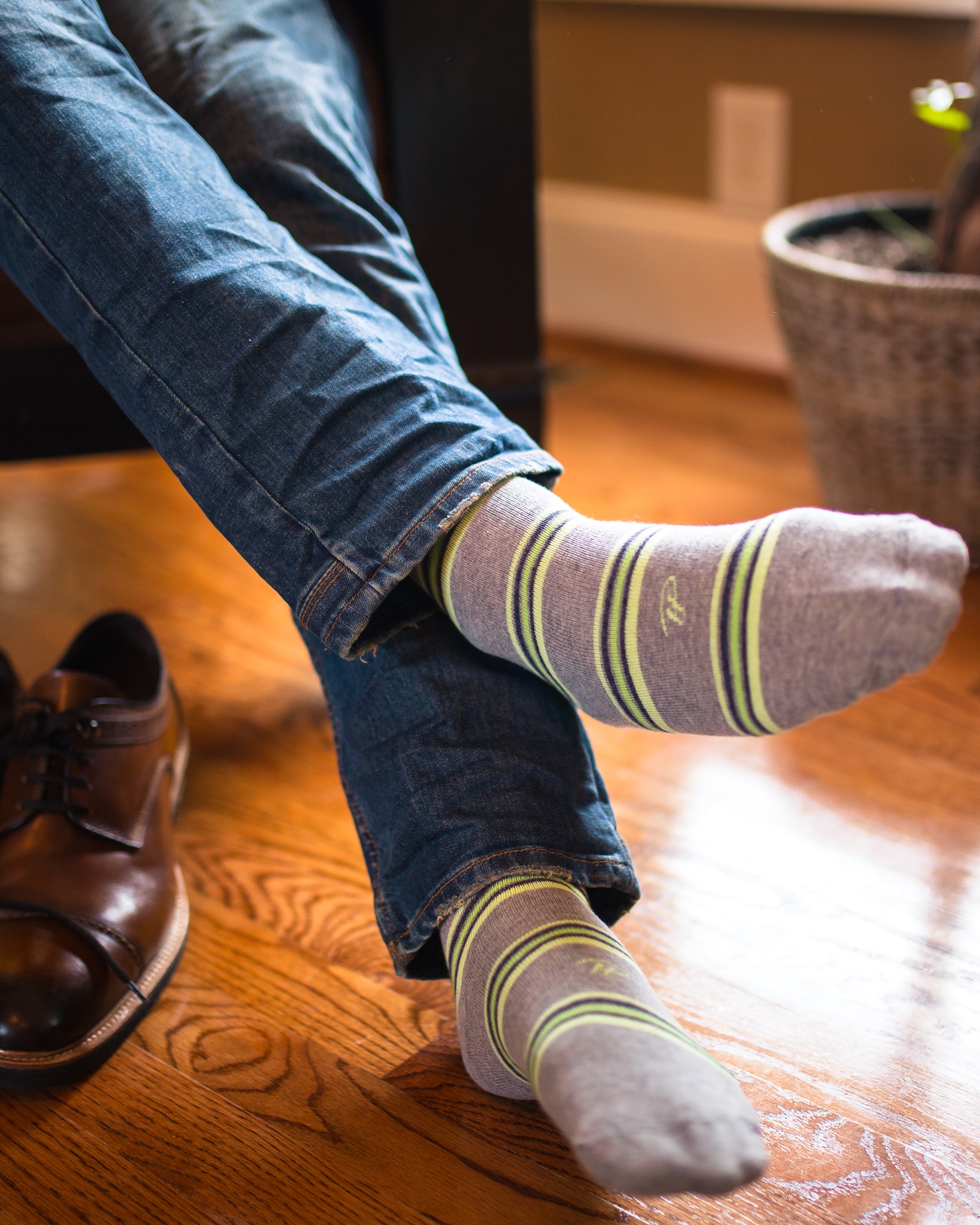 light grey over the calf dress socks with lime green stripes, legs crossed, blue jeans, brown dress shoes on floor