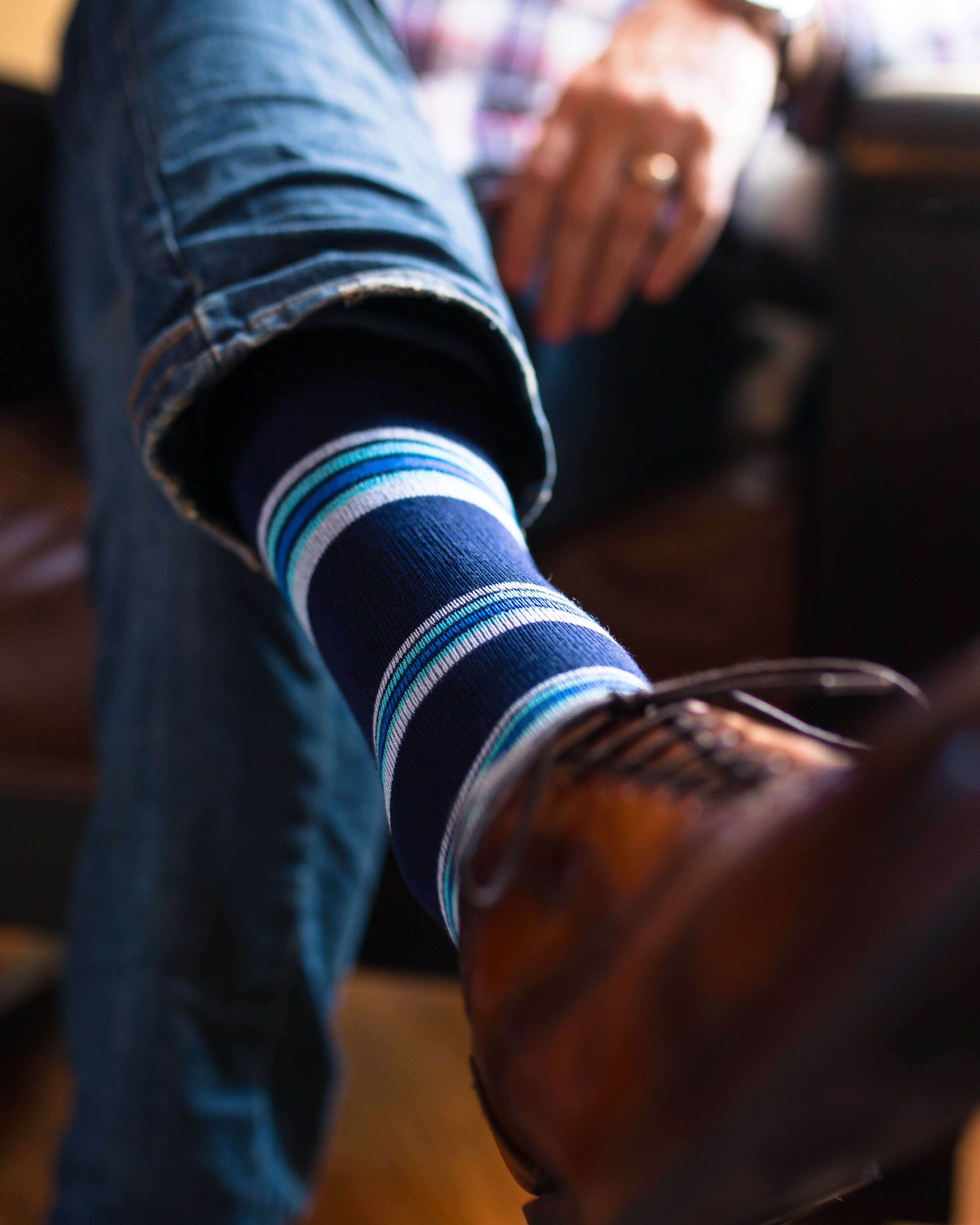 navy blue over the calf dress socks with light blue light pink and blue stripes, legs crossed, brown dress shoes, blue jeans