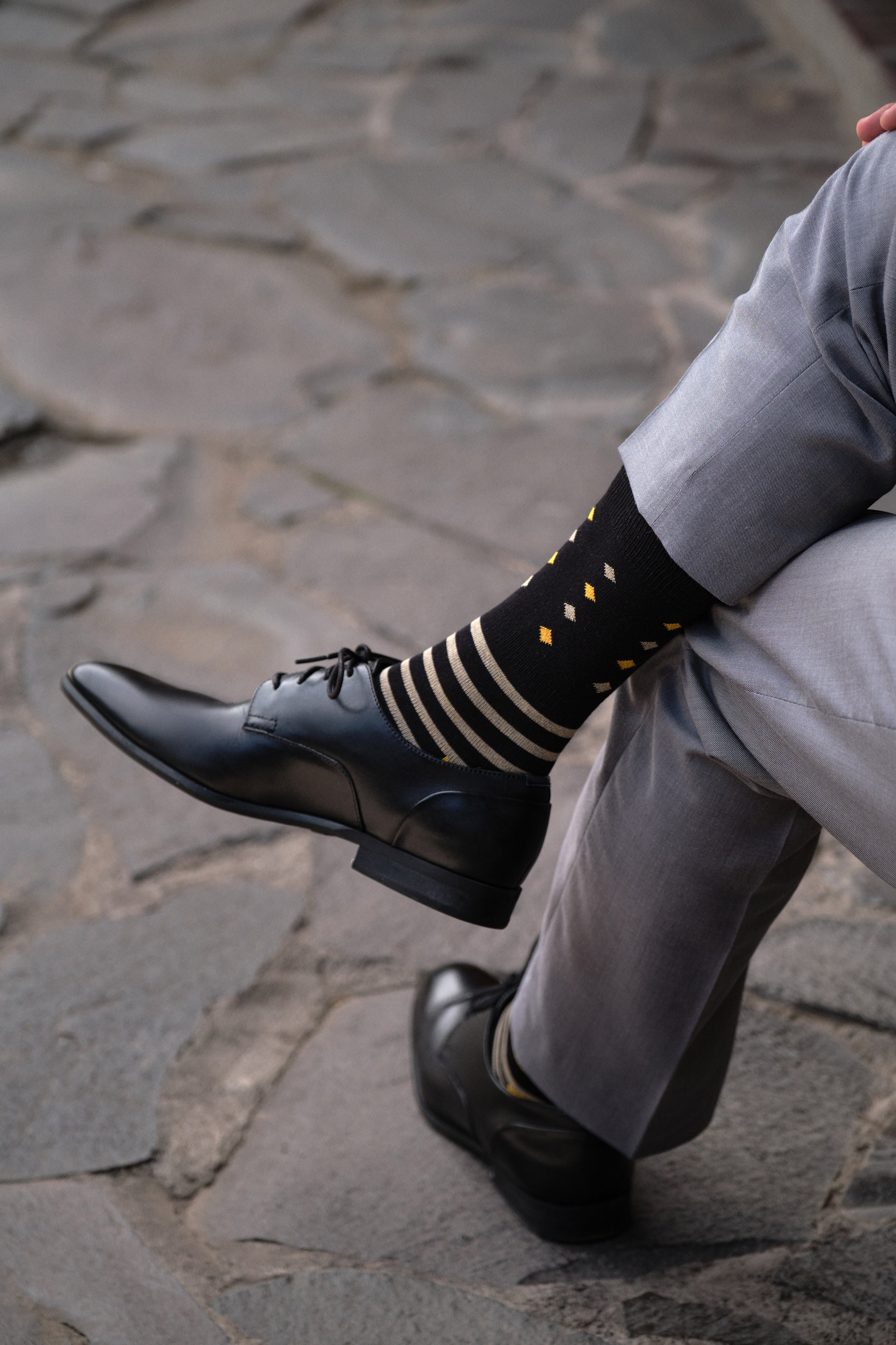 black mid calf dress socks with beige stripes and orange and beige prints, black dress shoes, grey dress pants