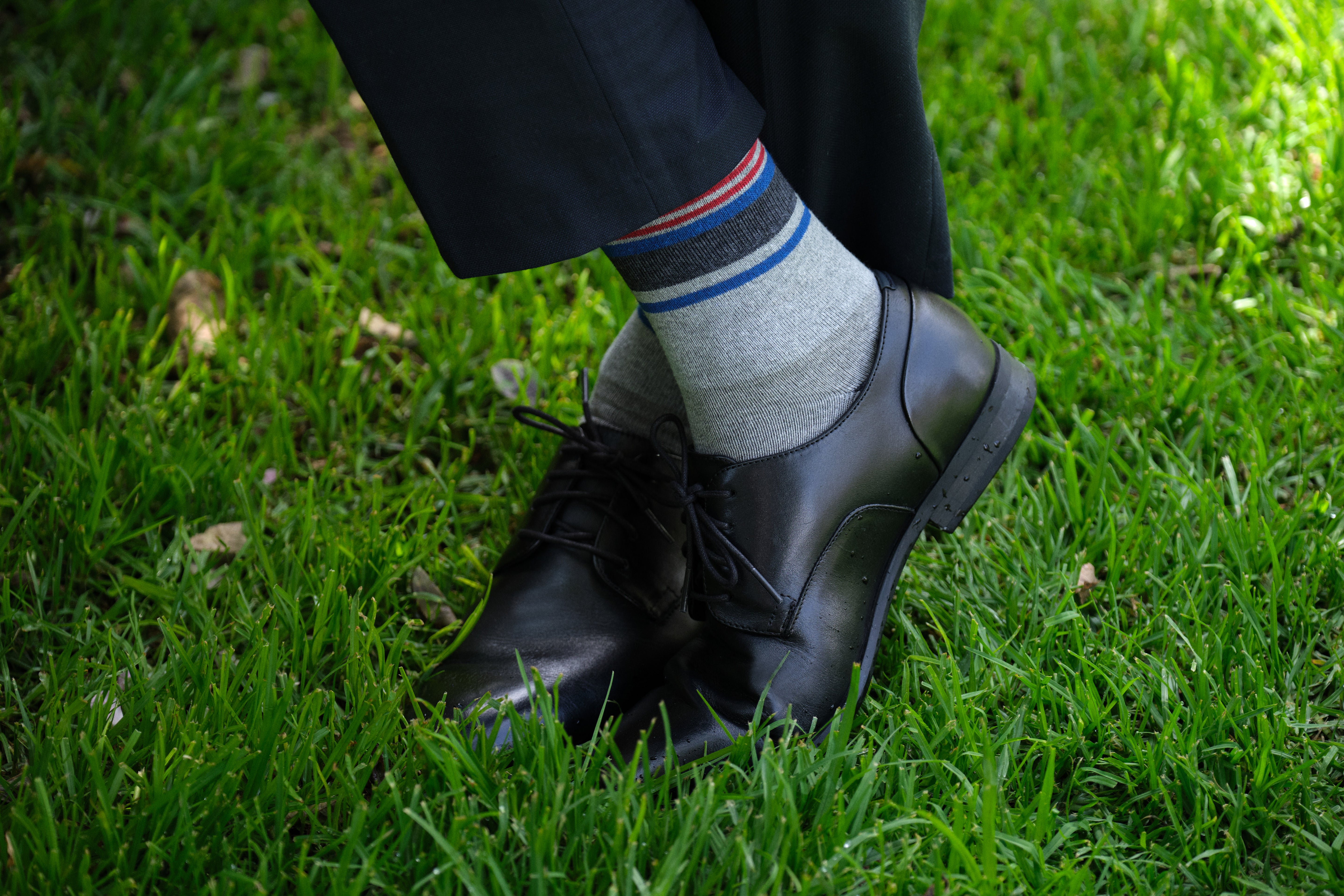 light grey mid calf dress socks with black blue and red stripes, black dress shoes, navy dress pants